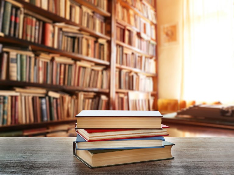 Stack of books on table at library proof it plus